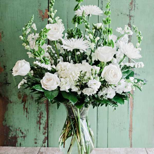 White roses and daisies arranged in a clear glass vase