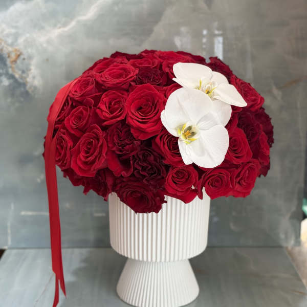 Red rose arrangement in a white pedestal vase with two white orchids