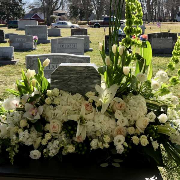 Large white funeral floral spray with lilies, roses, and orchids at a gravesite