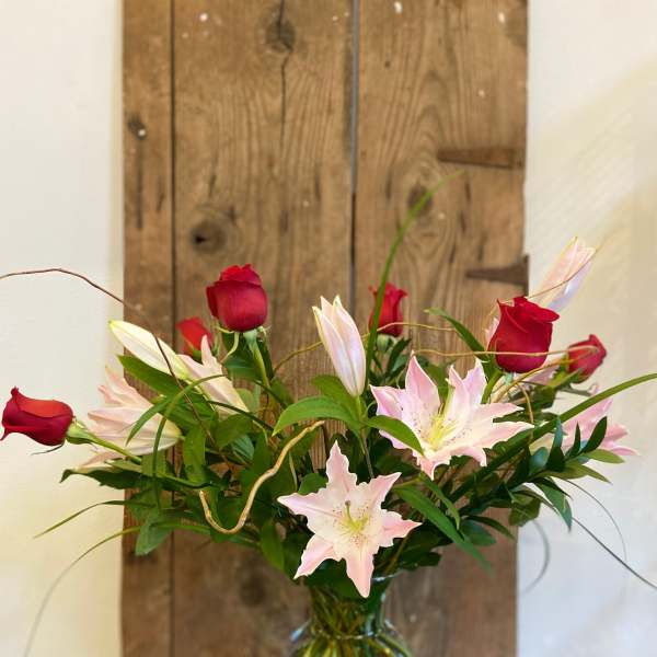Tall arrangement of red roses and light pink lilies in a clear glass vase