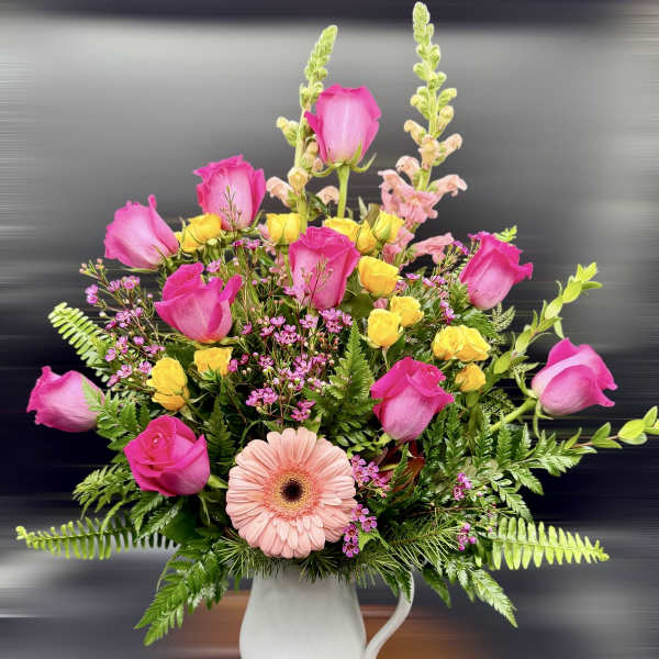 Pink roses and a peach gerbera daisy in a white pitcher vase