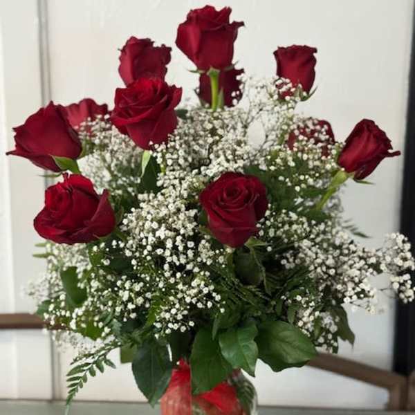 Red roses arranged with white baby's breath in a clear glass vase.