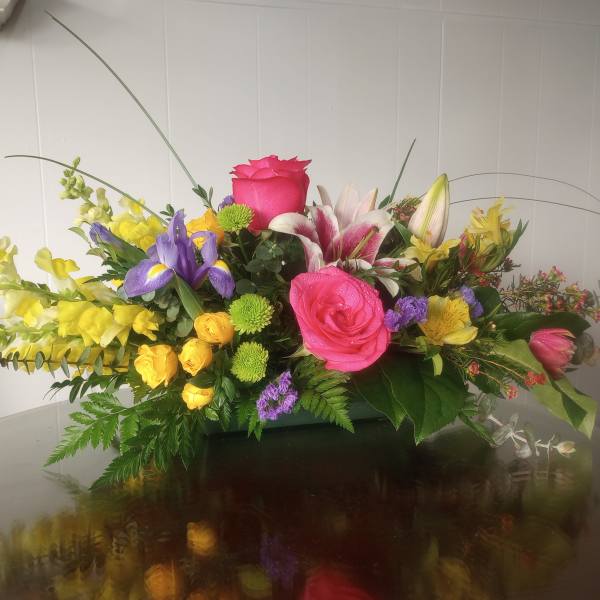 Colorful mixed flower arrangement with roses, lilies, and snapdragons in a low container