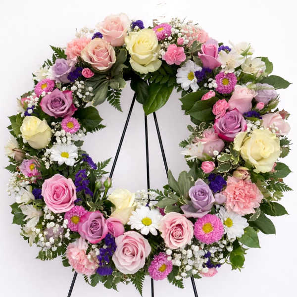 Pastel wreath of roses, daisies, carnations and filler flowers on a black easel stand