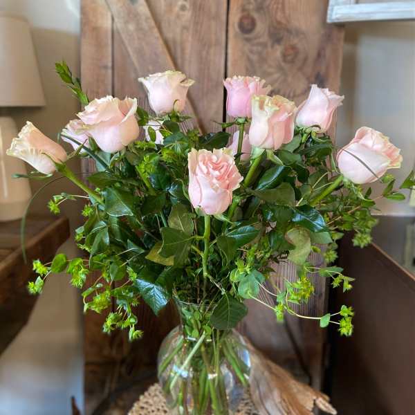 Tall arrangement of light pink roses with abundant foliage in a clear glass vase