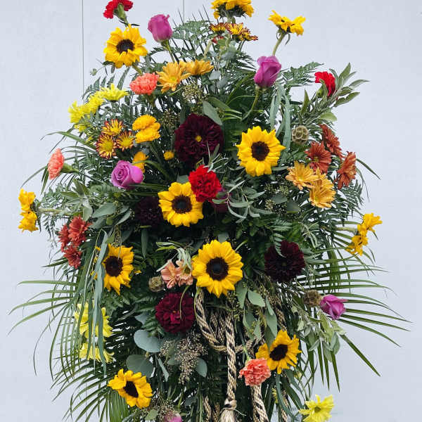 Tall floral standing spray with sunflowers, roses, and carnations on an easel