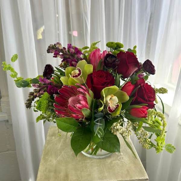 Mixed bouquet of red, pink, and green flowers in a clear glass vase