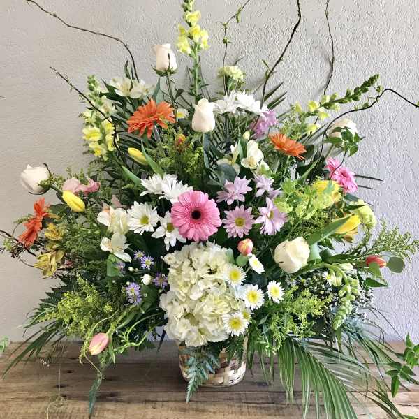 Large mixed flower arrangement in a woven basket with pink, white, yellow, and orange blooms
