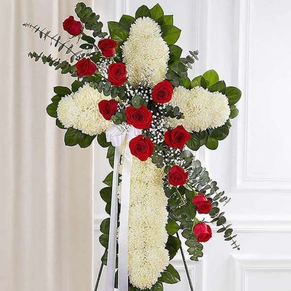 Cross-shaped floral tribute with white blooms and red roses on an easel
