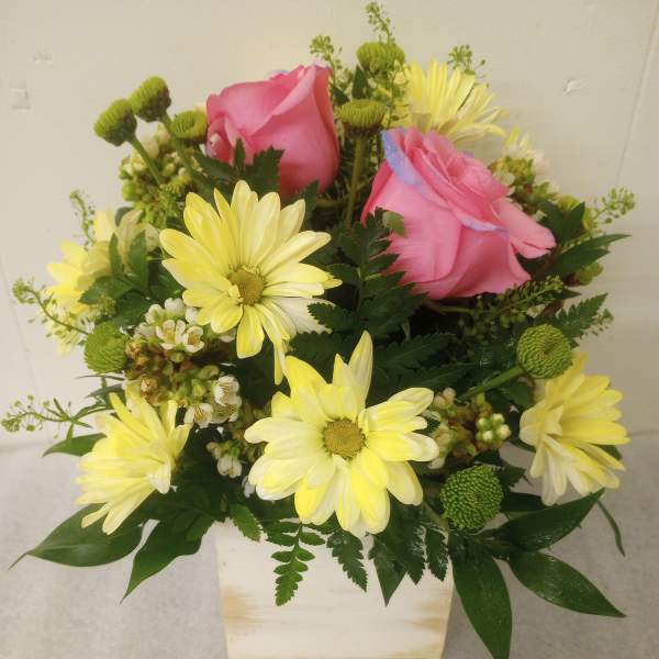 Pink roses and yellow daisies in a white square vase