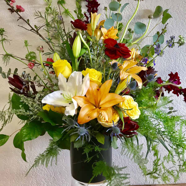 Tall mixed bouquet with lilies, roses, and red blooms in a black vase