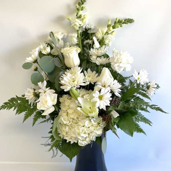 White floral arrangement in a dark vase with daisies, roses, and lilies