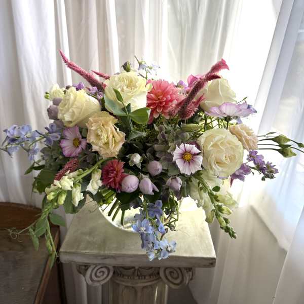 Mixed bouquet of cream, pink, and lavender flowers in a glass vase