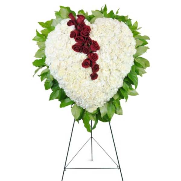 Heart-shaped standing spray of white flowers with a red rose cascade on a metal easel.