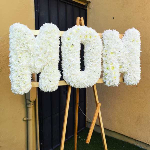 Large white floral letters spelling MOM displayed on a wooden easel.