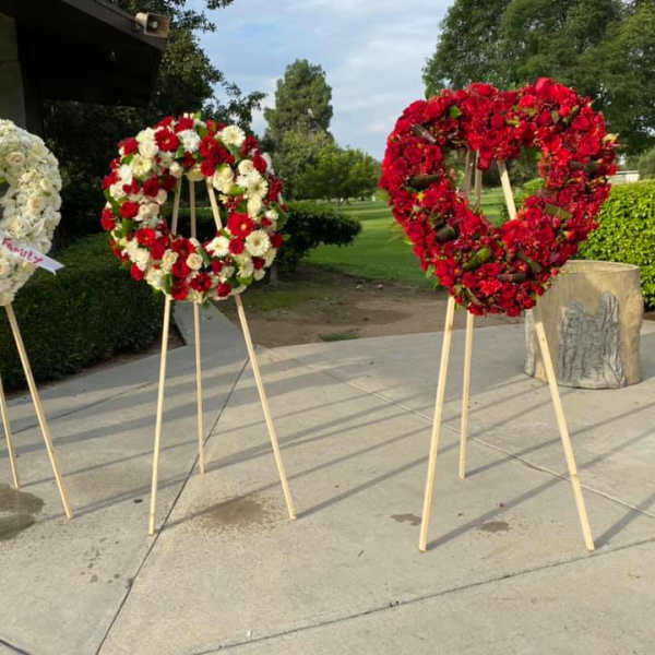 Three heart-shaped standing wreaths of white and red flowers on wooden easels outdoors