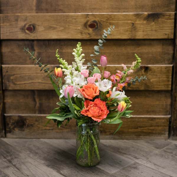 Mixed bouquet of pink, white, and orange flowers in a glass jar vase