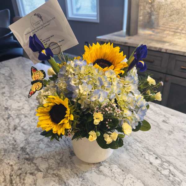 Sunflowers and blue irises in a white vase with a butterfly pick
