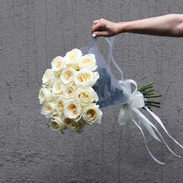 Hand holding a bouquet of white roses wrapped in sheer fabric