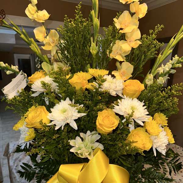 Yellow and white floral arrangement with a large yellow ribbon in a white vase