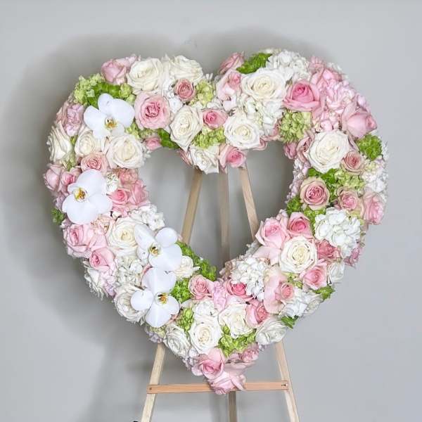 Heart-shaped floral wreath of pink and white roses with white orchids on an easel
