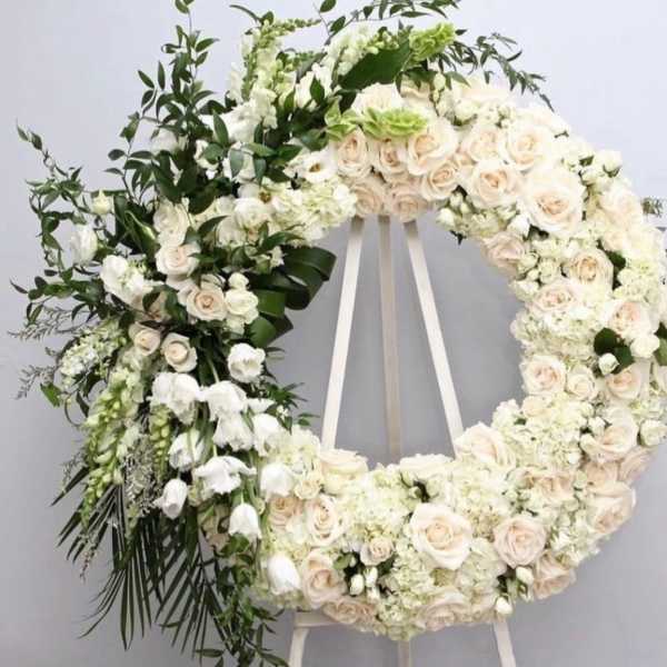 Large white floral wreath on a stand with cream roses and greenery