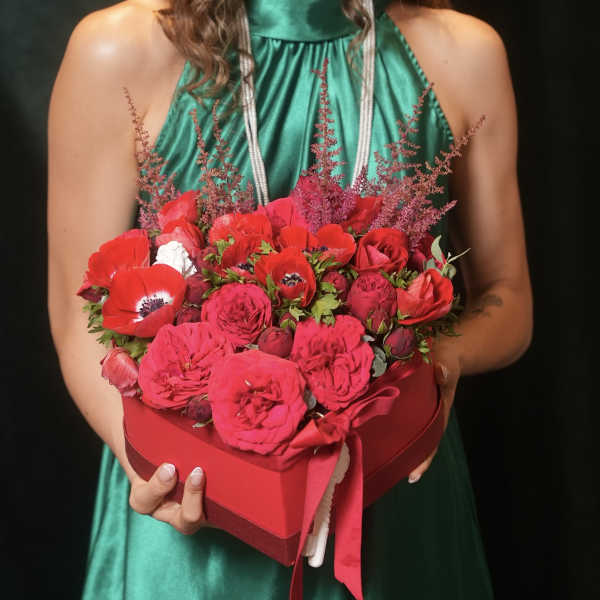 Heart-shaped box of red and pink flowers held by a woman in a green dress