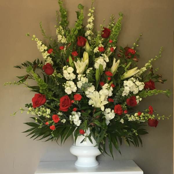 Large red, white, and green floral arrangement in a white urn vase