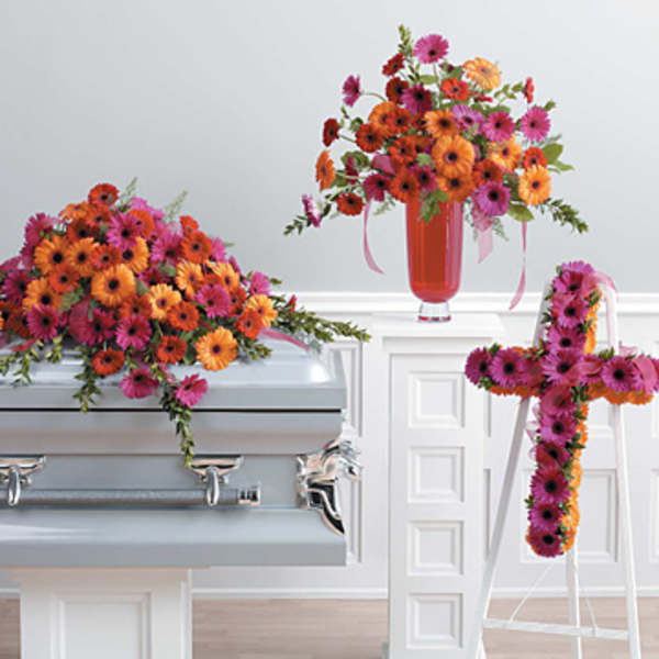 Bright gerbera daisy funeral arrangements on a casket and easel cross.