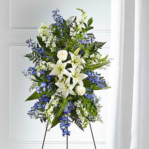 Tall standing floral spray with white lilies and blue flowers on an easel
