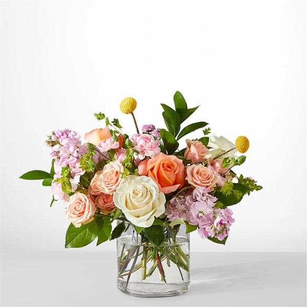 Bouquet of peach, white, and pink roses in a clear glass vase