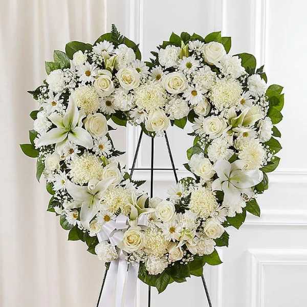 Heart-shaped standing wreath of white roses, lilies, and mums with ribbon on a metal easel