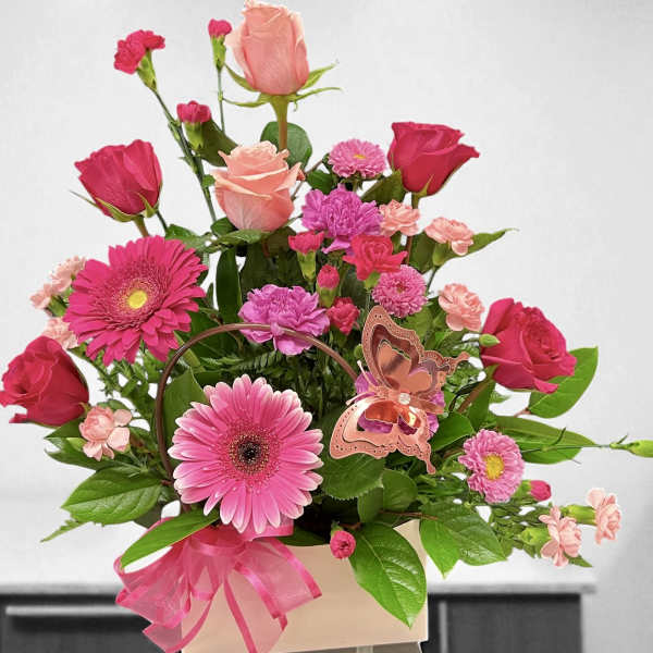 Pink and peach roses, gerbera daisies, and carnations in a pink box with a butterfly accent
