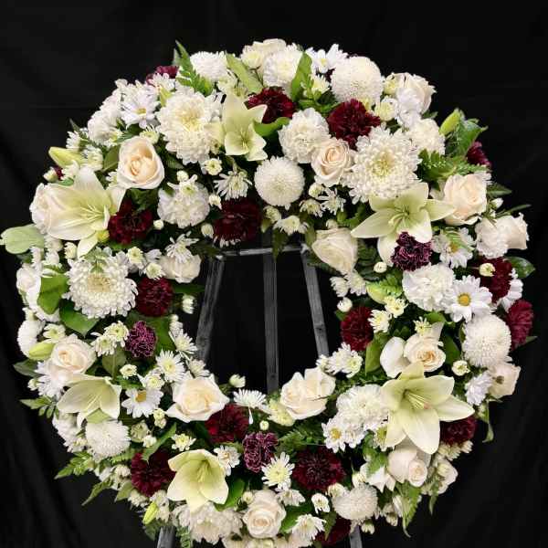 Large white and burgundy funeral wreath on a stand
