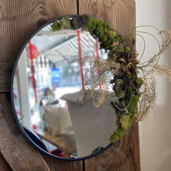 Round wall mirror with moss and dried foliage decorating one side of the frame