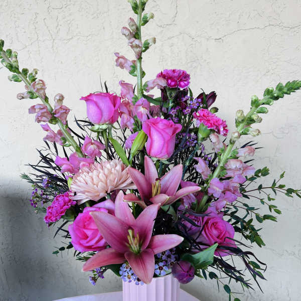 Pink roses and lilies in a white vase with purple accents