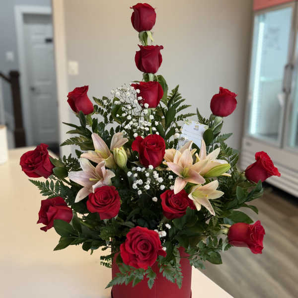 Red roses and pale lilies arranged in a red hatbox