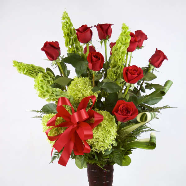 Red roses and green flowers in a tall vase with a red ribbon