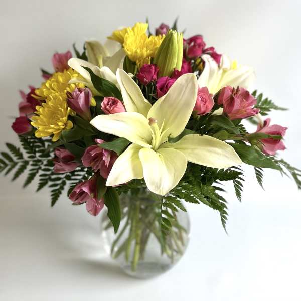 Bouquet of white lilies, pink flowers, and yellow chrysanthemums in a glass vase