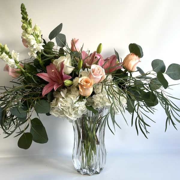 Pink lilies and roses in a clear glass vase with white blooms and greenery