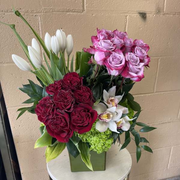 Mixed bouquet of pink and red roses with white tulips in a square vase