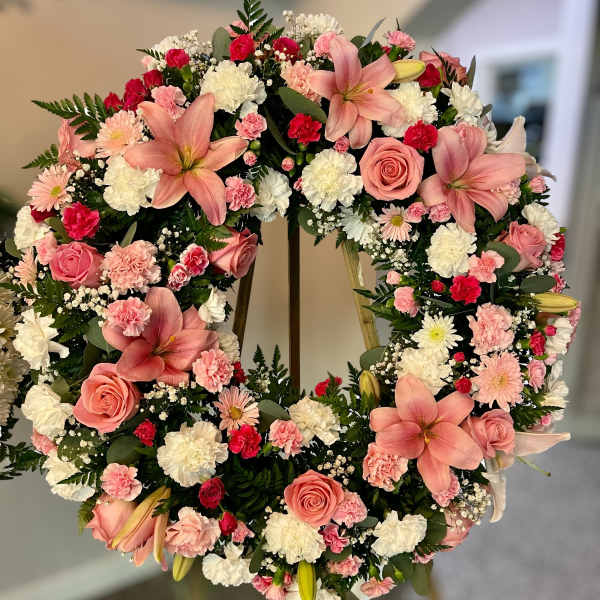 Standing wreath of pink lilies, roses, and mixed white and pink flowers on an easel