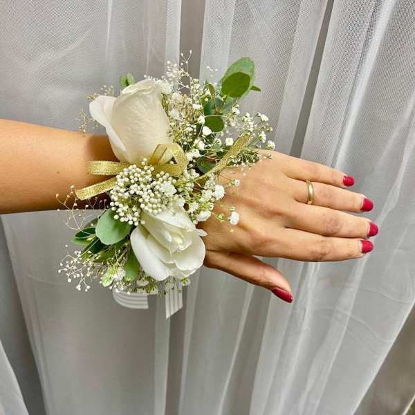 White floral wrist corsage with gold ribbon on a hand