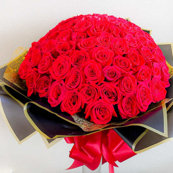 Large bouquet of red roses wrapped in black and gold paper with a red ribbon