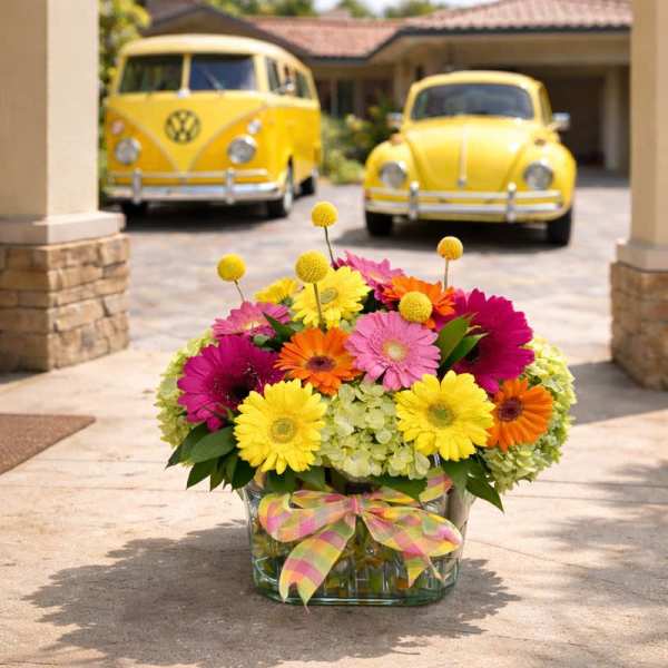 Bright mixed gerbera bouquet in a glass vase with a plaid ribbon
