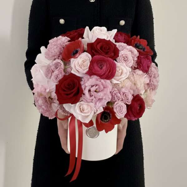 Round bouquet of red, pink, and white flowers in a white hatbox