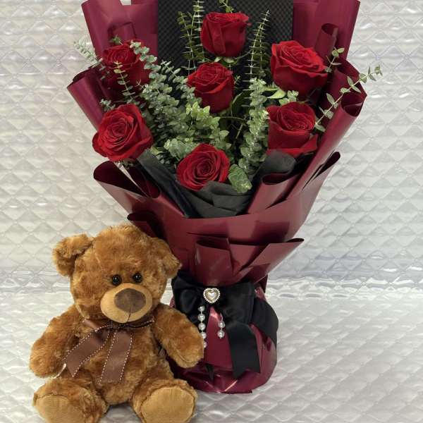 Bouquet of red roses with a teddy bear beside it