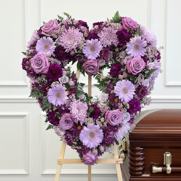 Heart-shaped purple floral tribute on an easel beside a casket