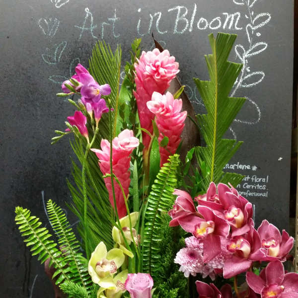 Tall tropical bouquet with pink orchids and green foliage in a black container