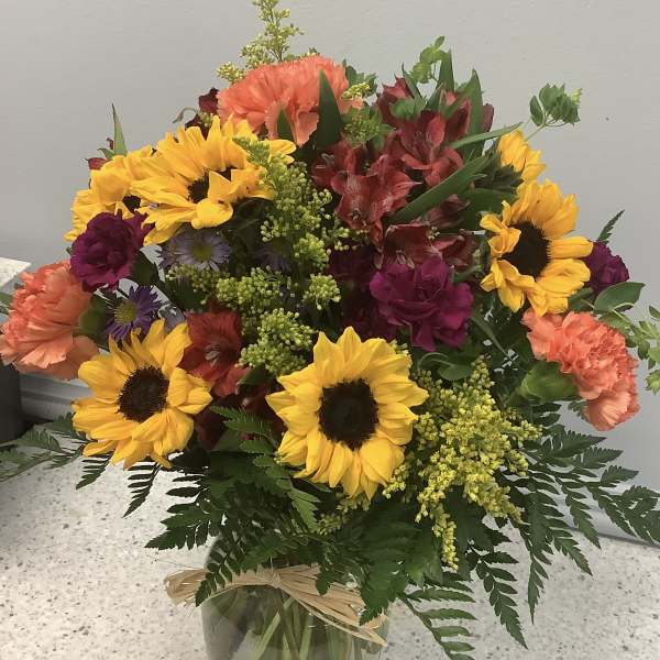 Mixed bouquet with sunflowers, carnations, and alstroemeria in a glass vase